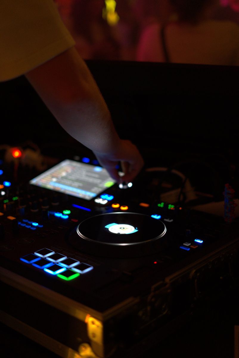 Hand des DJs am Pult mit leuchtenden Buttons und Plattenteller